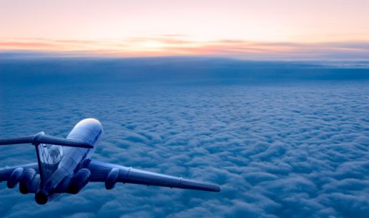 Paisagem aérea de avião à esquerda sobrevoando nuvens em meio as nascer do sol, alusivo ao combustível para aviação sustentável