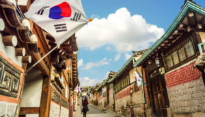 Bairro tradicional da Coreia do Sul com bandeira do país e céu azul com uma nuvem, alusivo à redução de emissões de carbono que o país pretende