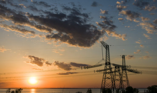 Torres de energia elétrica no lado direito, com linhas de transmissão atravessando a foto e pôr do sol ao fundo