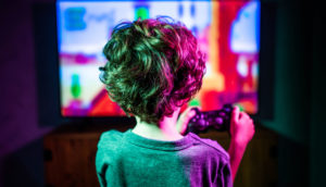 Criança de costas com controle na mão jogando videogame e TV ao fundo iluminada, alusivo ao Future 10