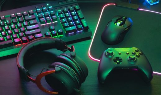 Teclado e mouse de computador, fone e controle de videogame, todos pretos e com detalhes iluminados, alusivo ao mercado de games