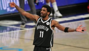 Kyrie Irving de braços abertos dentro de quadra de basquete com uniforme do Brooklyn Nets