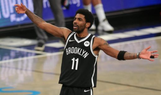 Kyrie Irving de braços abertos dentro de quadra de basquete com uniforme do Brooklyn Nets