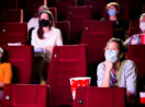 Pessoas de máscara dentro de cinema em poltronas vermelhas com pipoca e refrigerante, alusivo à Mostra Internacional de São Paulo