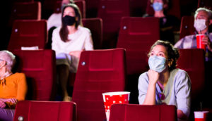 Pessoas de máscara dentro de cinema em poltronas vermelhas com pipoca e refrigerante, alusivo à Mostra Internacional de São Paulo