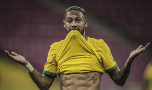 Neymar Jr. com o uniforme da seleção brasileira, puxando a camisa pela boca e fazendo gesto de dúvida com as mãos