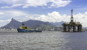 Plataforma de petróleo e navio petroleiro lado a lado com o Rio de Janeiro ao fundo, alusivo à previsão de oferta da Opep para o Brasil