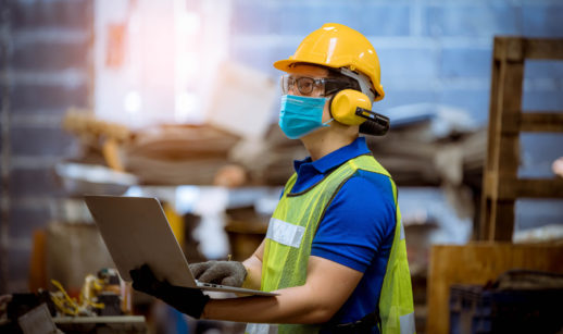 Trabalhador com laptop nas mãos, capacete e colete, alusivo à produção industrial