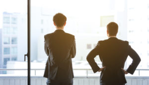 Dois executivos de terno preto, de costas, olhando por janela iluminada, alusivo ao Safra Report de outubro