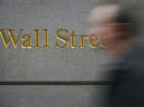 Foto de parede com destaque para Wall Street e pessoa passando em frente borrada, alusivo à carteira Safra Top 10 BDRs