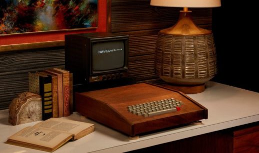 Computador Apple-1 sobre mesa antiga com abajur e livro ao lado
