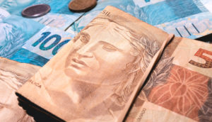 Cédulas e moedas de real sobrepostas, alusivo ao pagamento do Auxílio Brasil