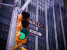 Semáforo com sinal verde em primeiro plano e placa com direções para Wall Street, alusivo aos BDRs para investir em novembro