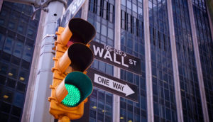 Semáforo com sinal verde em primeiro plano e placa com direções para Wall Street, alusivo aos BDRs para investir em novembro