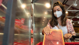 Mulher com a porta da geldadeira de mercado aberta colocando carne dentro do carrinho, alusivo à Black Friday