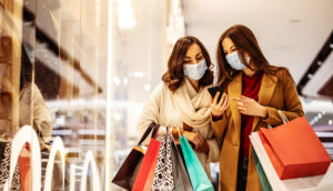 Duas mulheres de máscara e com sacolas nas mãos fazendo compras em shoppings com a Black Friday