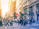 Pessoas caminhando juntas por rua de Nova York, nos EUA, alusivo a onde investir com a inflação global acomodada