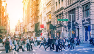 Pessoas caminhando juntas por rua de Nova York, nos EUA, alusivo a onde investir com a inflação global acomodada