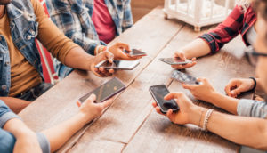 Pessoas com celulares nas mãos juntas sobre mesa de madeira, alusivo à entrada de novos participantes no mercado com o leilão do 5G
