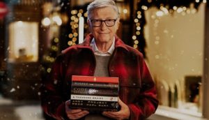 Bill Gates, com casaco vermelho xadrez escuro, segurando os livros recomendados por ele de 2021