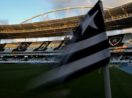 Close de bandeira de escanteio com as cores e a estrela do Botafogo com o Estádio Nilton Santos ao fundo