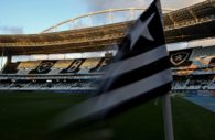 Close de bandeira de escanteio com as cores e a estrela do Botafogo com o Estádio Nilton Santos ao fundo