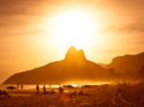 Praia de Ipanema, no Rio de Janeiro, com o Morro Dois Irmãos ao fundo, com sol raiando, alusivo à prevenção ao câncer de pele