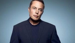 Elon Musk, de camiseta azul escura com paletó por cima, de cabeça caindo para a direita, sem sorrir