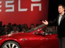 Elon Musk, de pé, com carro da Tesla atrás, durante apresentação de modelo à plateia