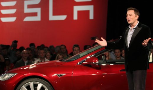 Elon Musk, de pé, com carro da Tesla atrás, durante apresentação de modelo à plateia