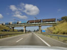 Vista de dentro de carro para trem sobre rodovia, alusivo ao avanço das ferrovias no Brasil