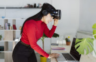Mulher com óculos de realidade virtual olhando para tela de laptop, alusivo à inteligência artificial no marketing e nas vendas