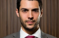 Lucas Prediger, executivo da Sami Saúde, olhando sem sorriso, com terno cinza e gravata vinho