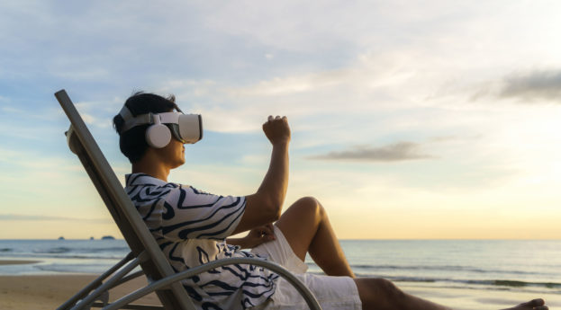 Homem sentado em cadeira na praia com óculos de realidade virtual, fazendo reunião no metaverso