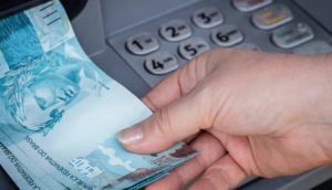 Mão de pessoa segurando maços de notas de R$ 100, alusivo aos saques da poupança em novembro
