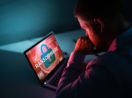 Homem olhando com as mãos no queixo para tela de PC com o escrito "ransomware", com destaque para o fundo na cor vermelha