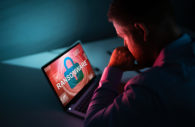 Homem olhando com as mãos no queixo para tela de PC com o escrito "ransomware", com destaque para o fundo na cor vermelha