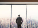 Homem executivo de costas olhando por vidro de prédio, alusivo à carteira Safra Top 10 Ações de dezembro