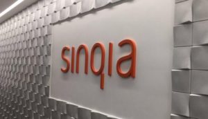 Letreiro escrito "Sinqia" em laranja em parede branca atrás