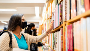 Mulher de máscara em livraria olhando prateleiras, alusivo às vendas de livros no Brasil