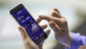 Mão de pessoa com smartphone aberto em tela de bolsa de valores, alusivo ao ato de investir em dividendos