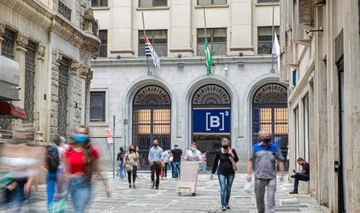 Prédio da B3, a bolsa brasileira, visto de fora, com destaque para o logo em azul e branco, com pessoas andando nas calçadas desfocadas, alusivo à entrada de capital estrangeiro
