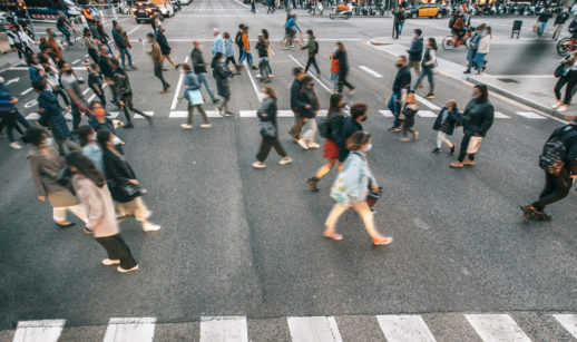 Aérea de pessoas com máscara atravessando faixa de pedestres, alusivo aos novos casos de covid-19 no mundo