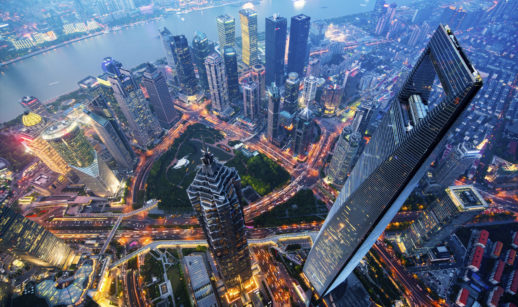 Aérea da cidade de Xangai, uma das zonas de testes de blockchain na China, com diversos prédios futuristas e iluminados, à noite