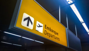 Letreiro amarelo de aeroporto preso ao teto com os dizeres "Embarque" e "Departures", alusivo à FlyBy