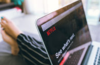 Laptop com a tela aberta no sistema da Netflix, sobre o colo de uma pessoa de pijama