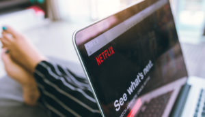 Laptop com a tela aberta no sistema da Netflix, sobre o colo de uma pessoa de pijama