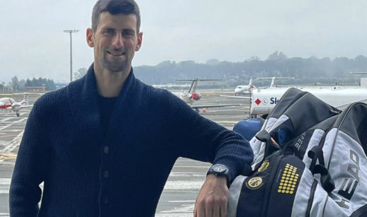 Novak Djokovic, tenista sérvio com suéter preto e braço esquerdo apoiado sobre monte de malas em aeroporto