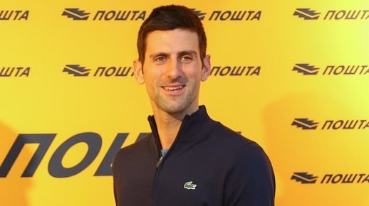 Novak Djokovic sorrindo com suéter azul e fundo amarelo