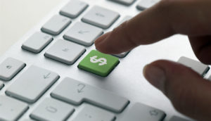 Dedo de uma pessoa apontando para tecla verde com cifrão de dinheiro em teclado branco, alusivo ao Tesouro Direto